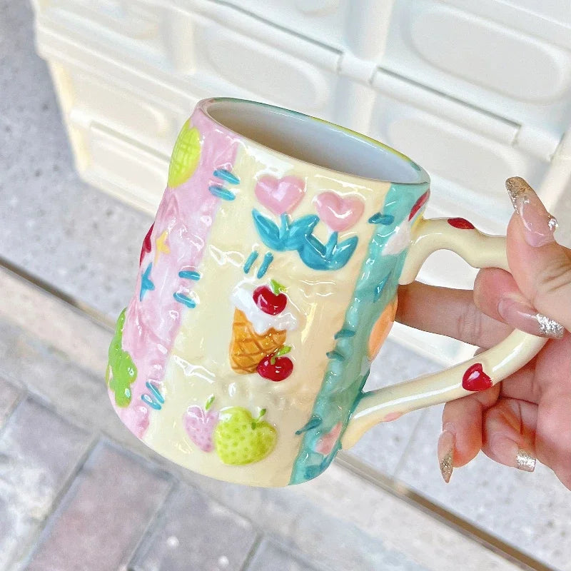 Colorful mug with floral and fruit designs held by a hand on a light background