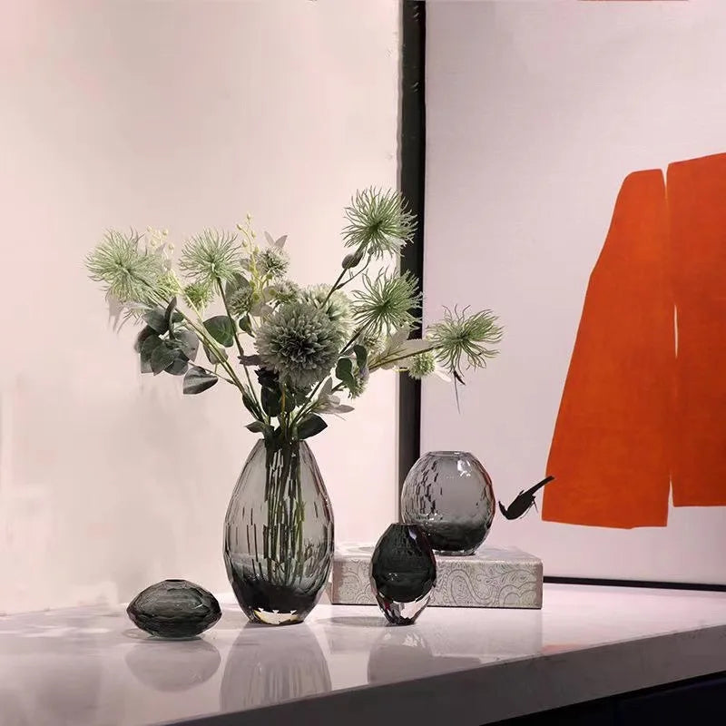 Decorative smoked glass vases with flowers on a surface, with abstract art in the background.