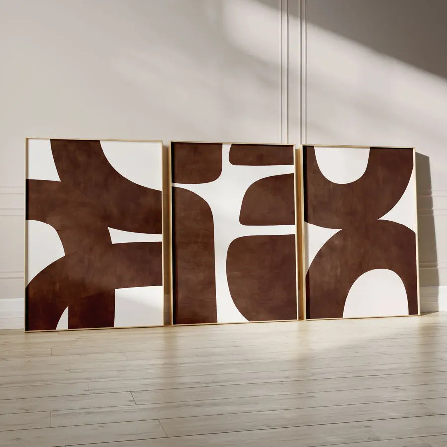 Three abstract wall art pieces with brown and white design on a light wooden floor.
