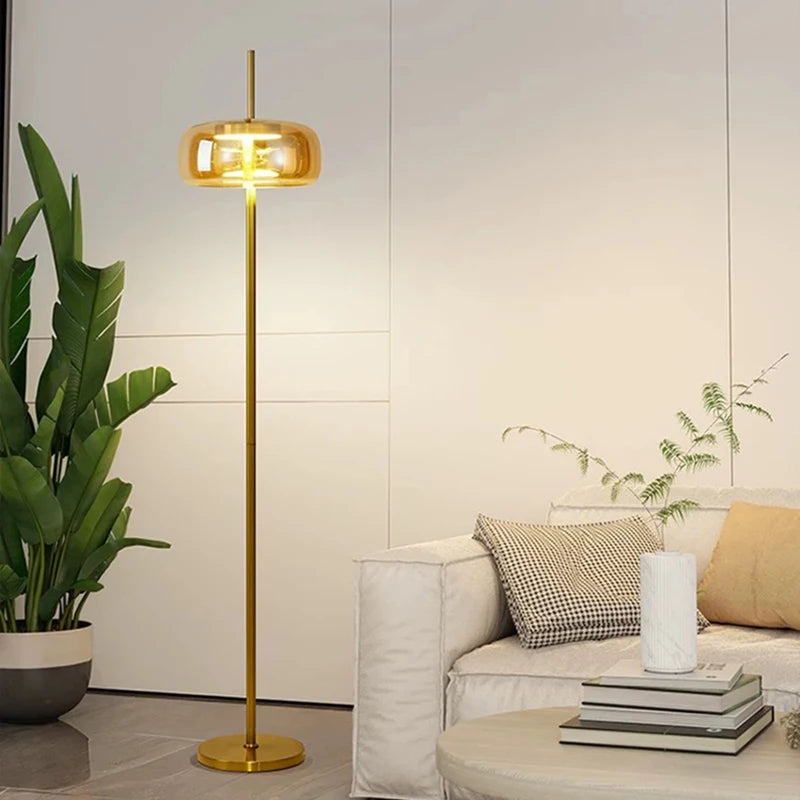 Minimalist gold floor lamp with amber glass shade lit in a warm glow.