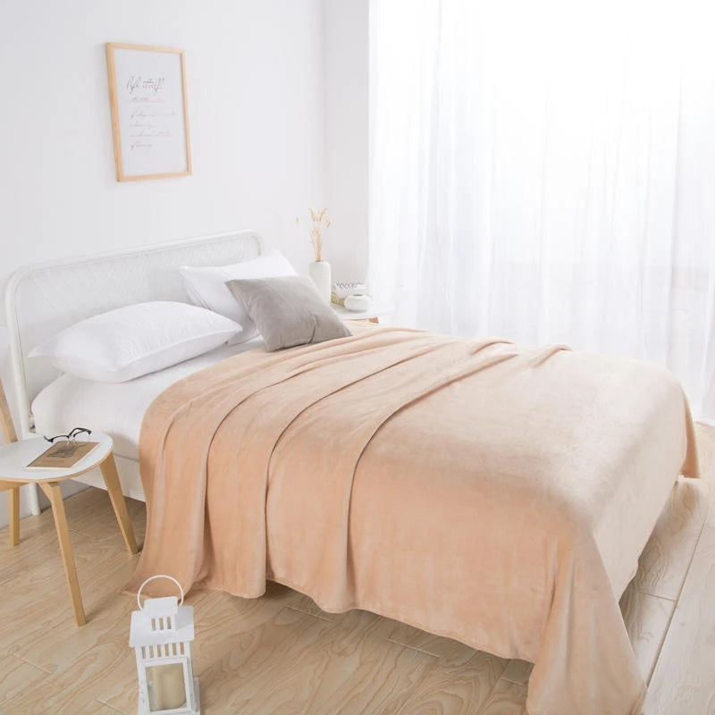 Beige plush blanket on a white bed with a grey cushion