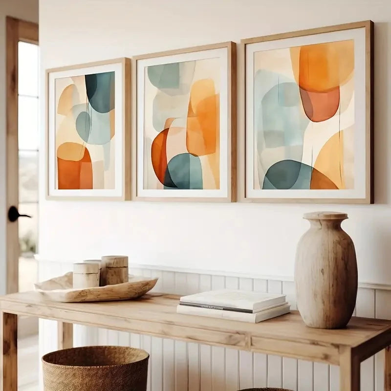 Three abstract art pieces on a wall above a wooden console table with decor items.