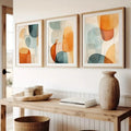 Three abstract art pieces on a wall above a wooden console table with decor items.
