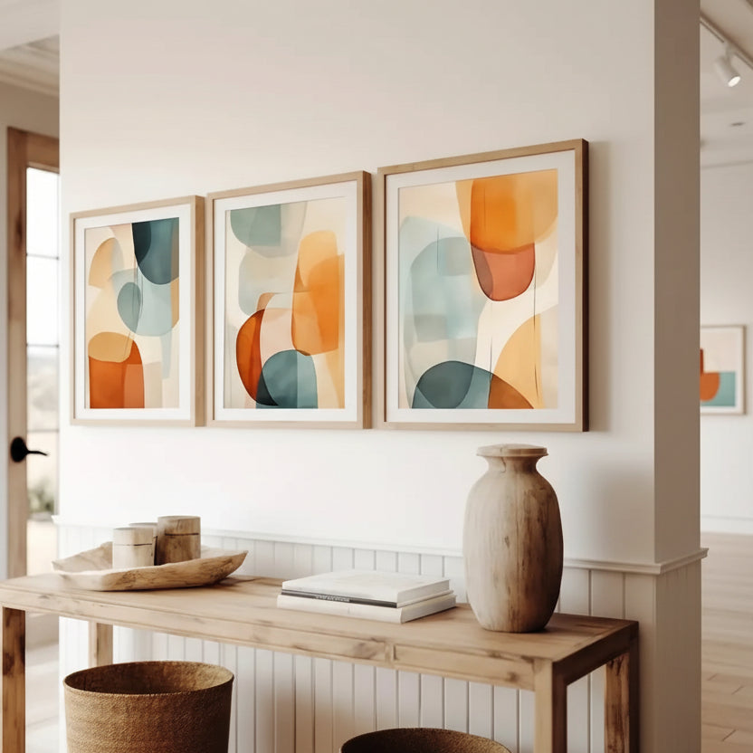 Three abstract art pieces on a wall above a wooden console table with decor items.