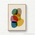 Framed abstract art print with colorful shapes on a white brick wall.
