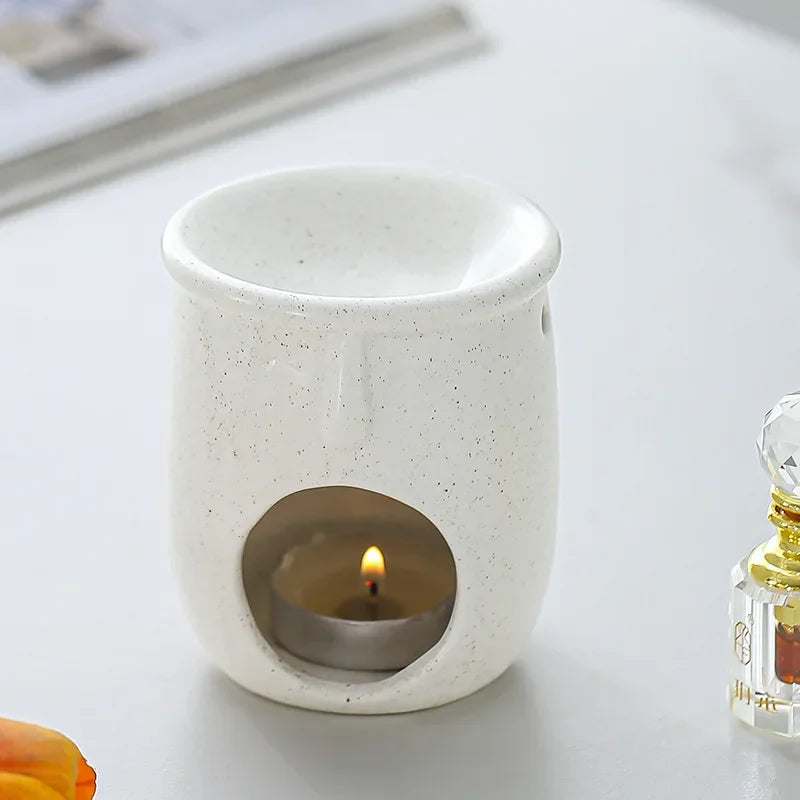 White ceramic oil burner with a lit candle inside on a light surface.