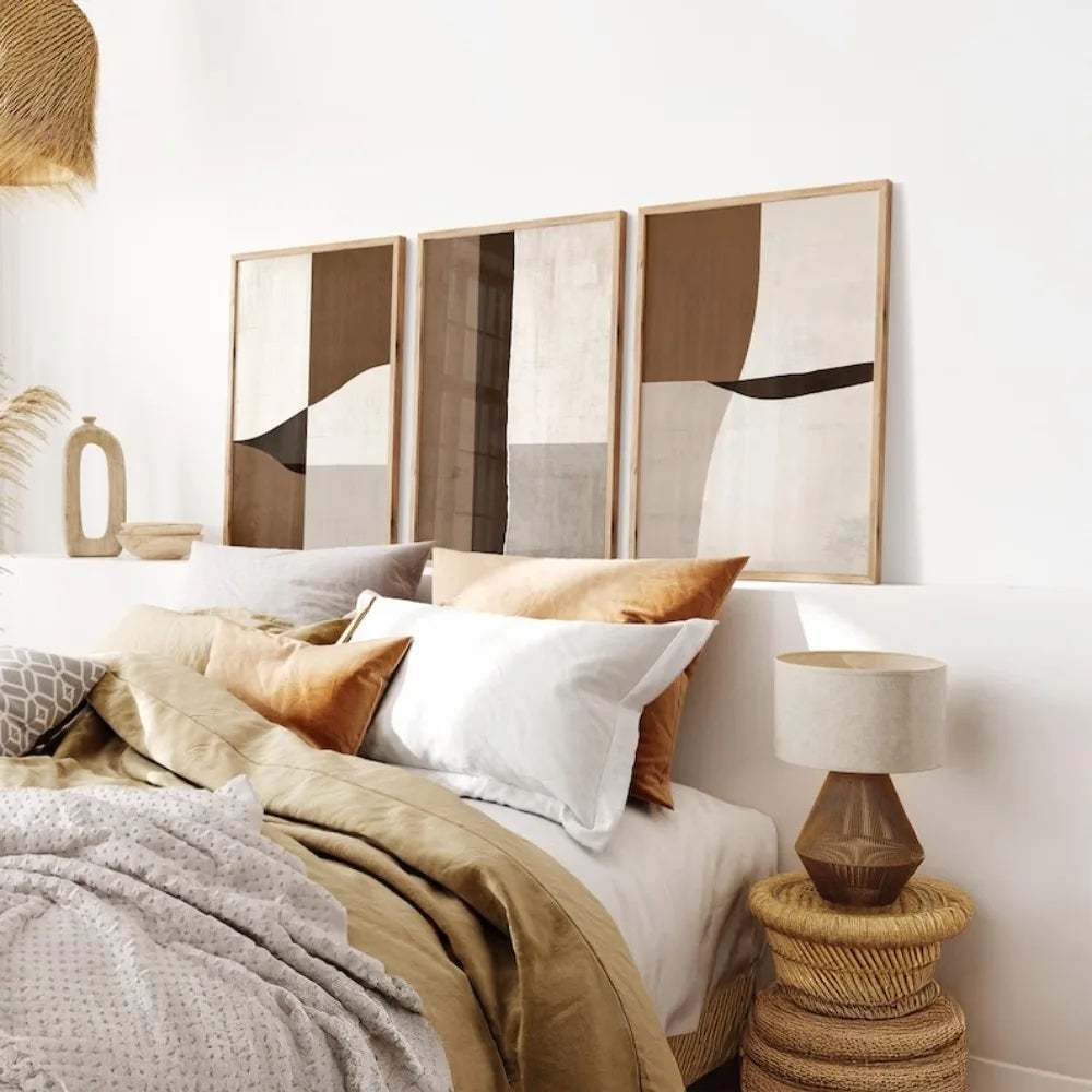 Cosy bedroom with abstract wall art, pillows, and a lamp on a woven side table.