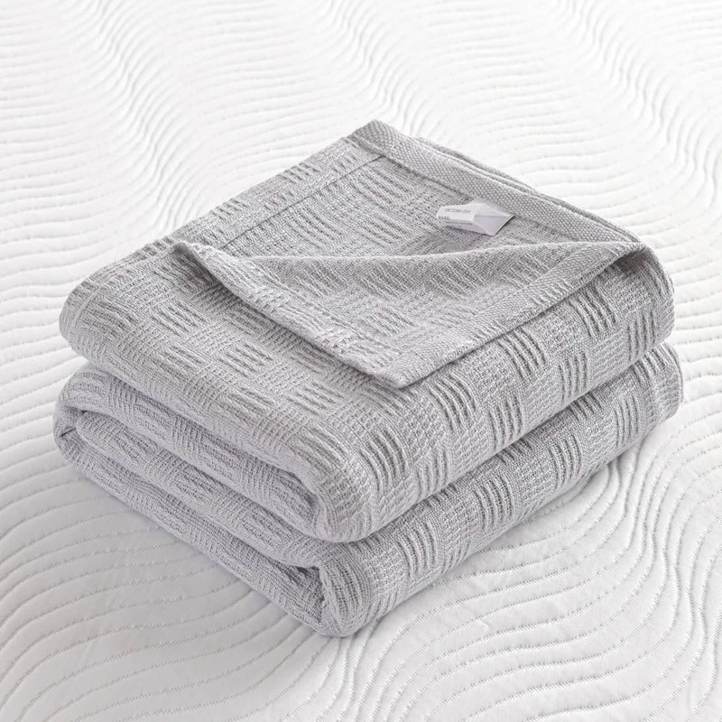 Folded silver grey knit throw blanket with open weave pattern and care label on white bed.