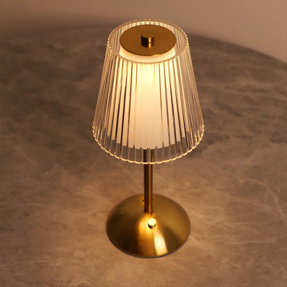 Gold table lamp with pleated glass shade on a textured surface