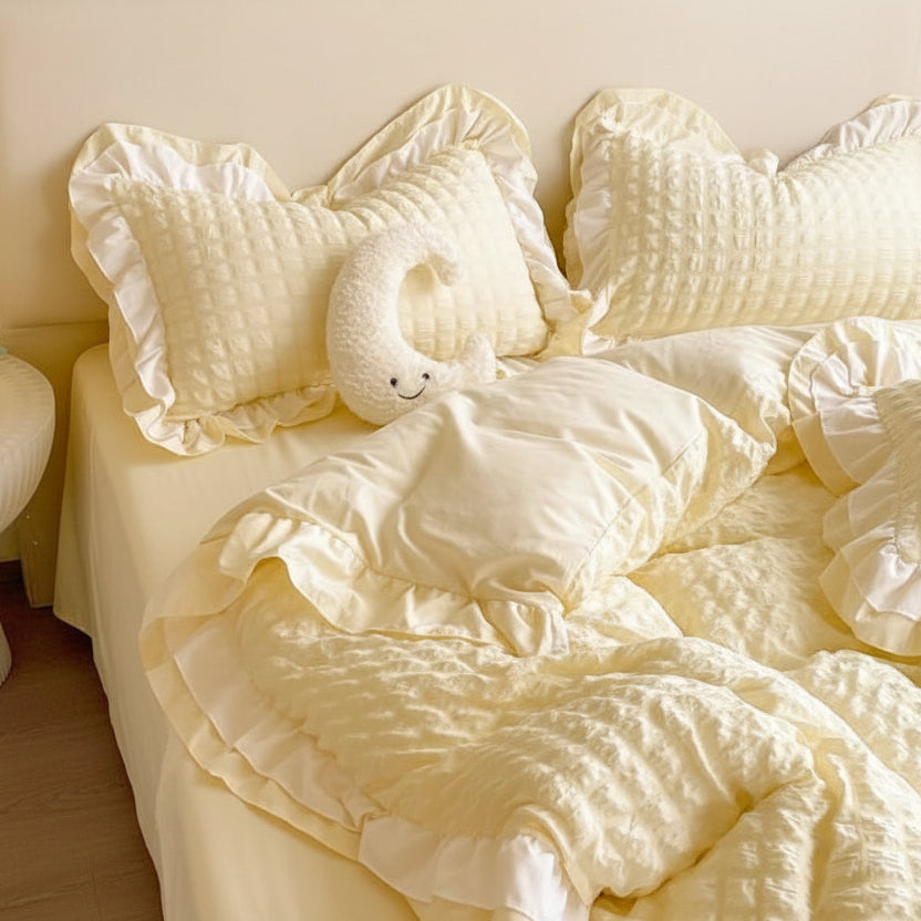 Cream-colored bedding set on a bed with a side table and plant in the background.