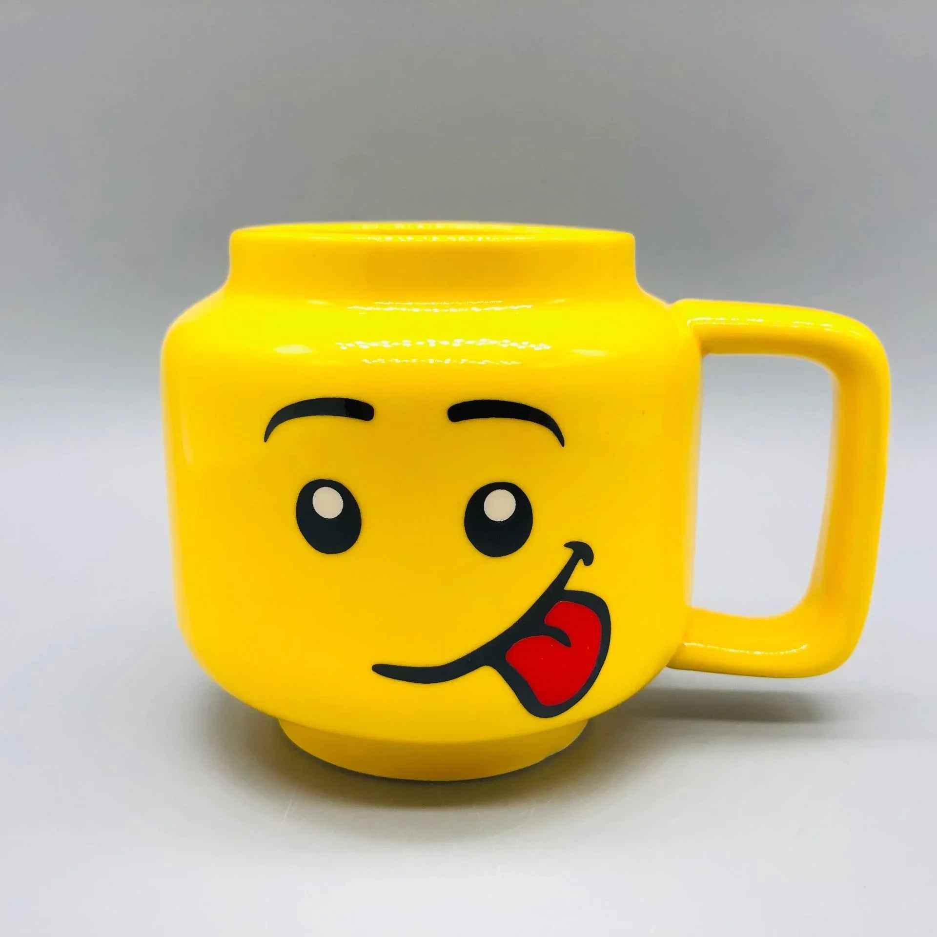 Yellow mug with a tongue face design on a grey background