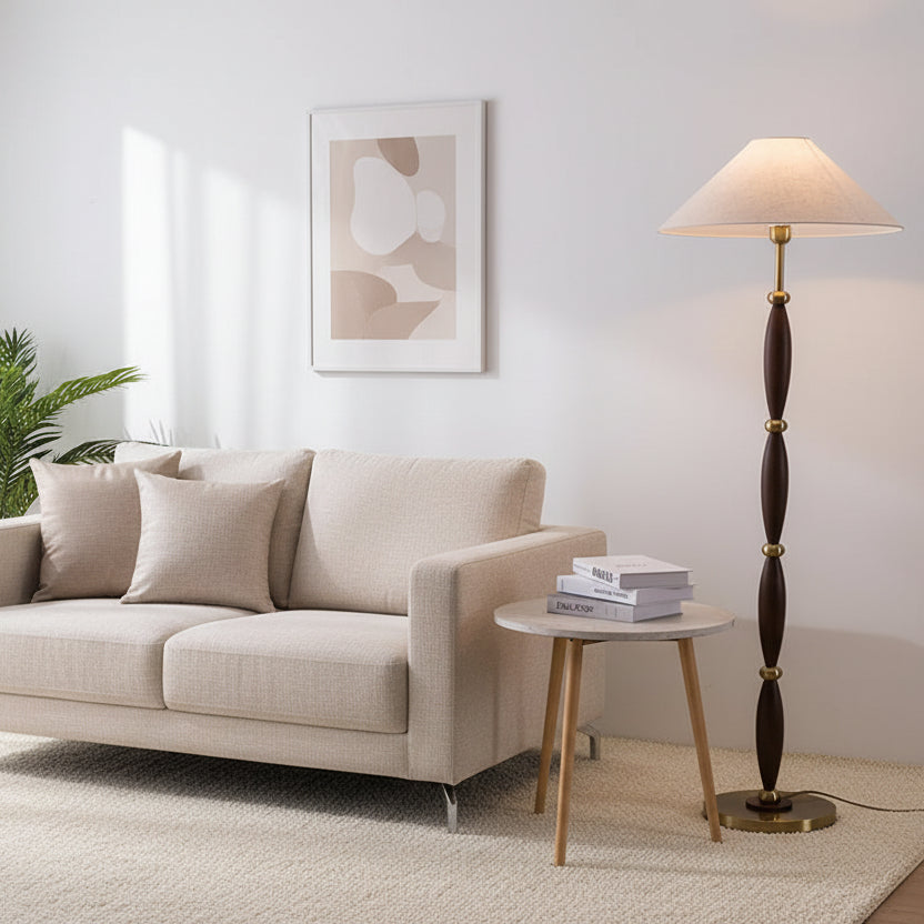 Floor lamp with wooden and brass design next to a small table with books against a plain wall.