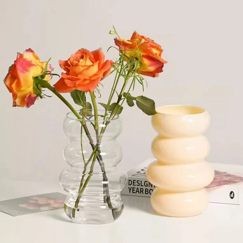 Clear glass vase with orange and yellow flowers next to a beige spiral vase on a light surface.