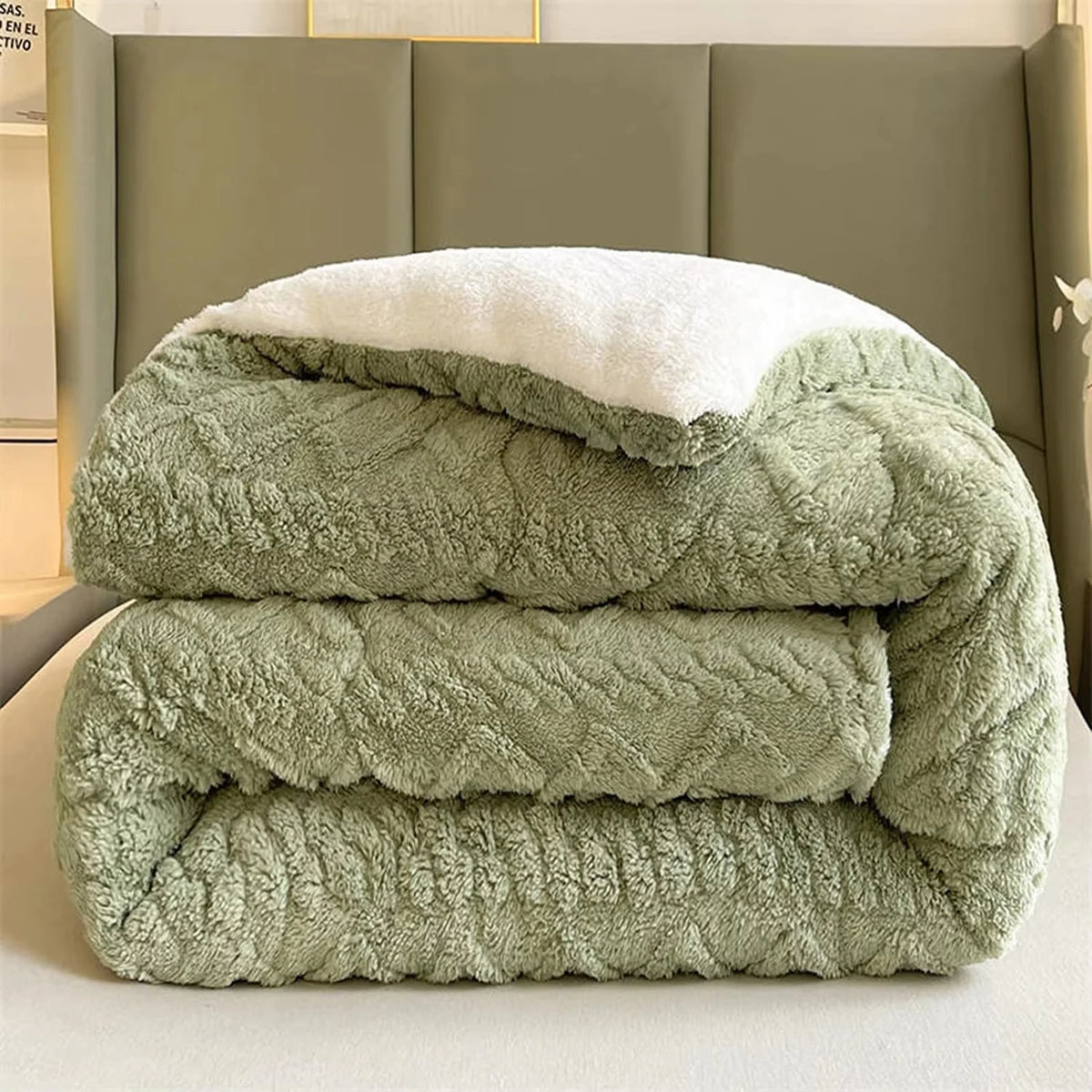 Folded green textured blanket on a bed with a neutral headboard.