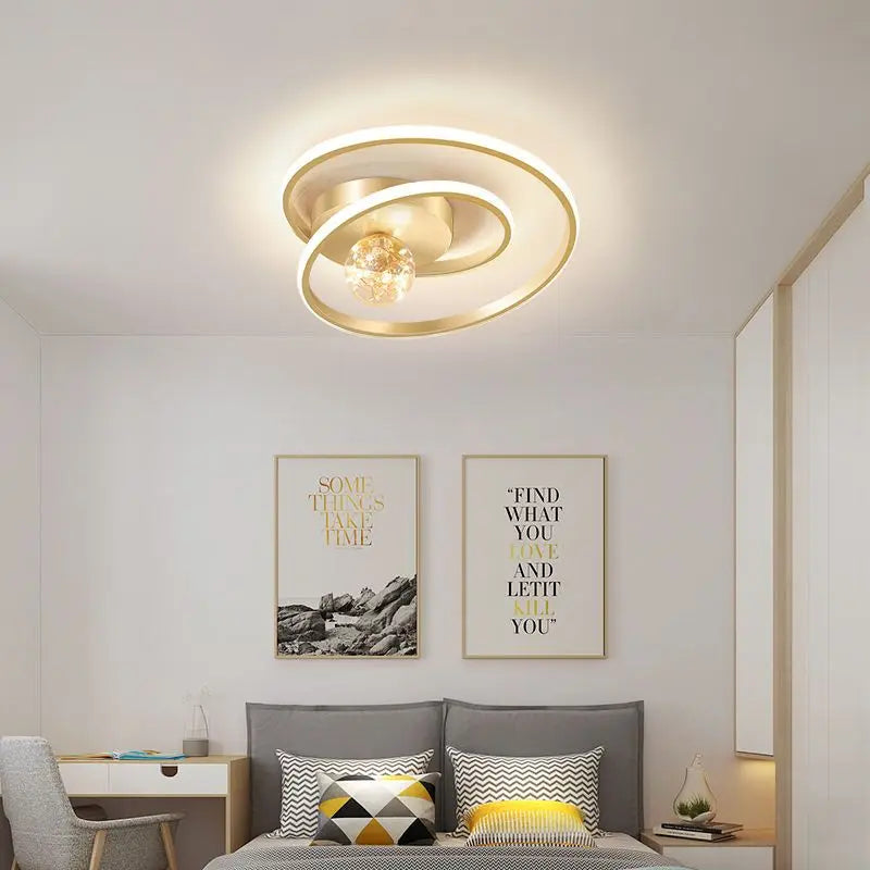 Gold Nordic spiral ceiling light with amber glass globe installed above a modern bedroom with warm ambient lighting