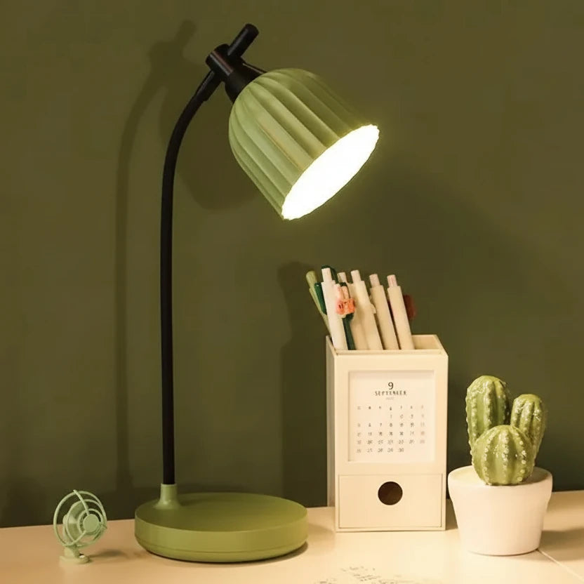 Green desk lamp on a table with a calendar and cactus plant against a dark green background