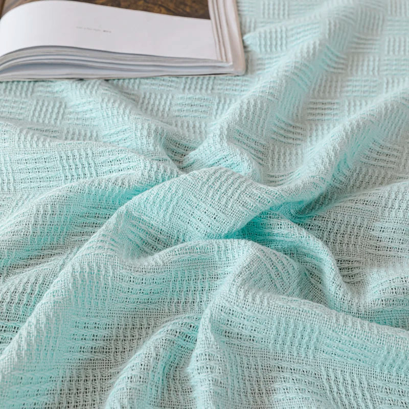 A mint green cotton knit blanket with textured basket weave on white quilted surface