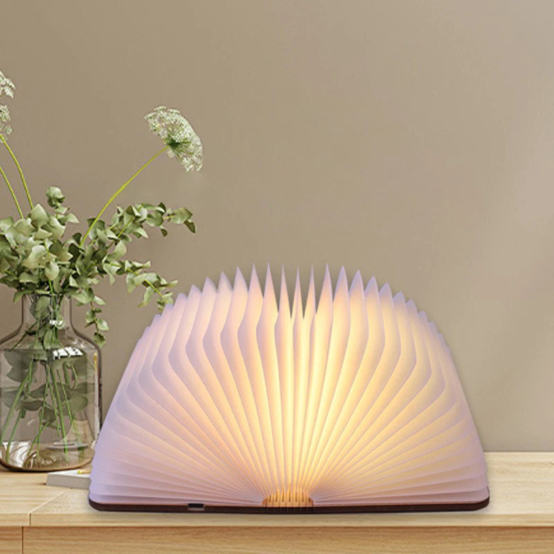Book-shaped lamp on a wooden surface with a vase of flowers in the background