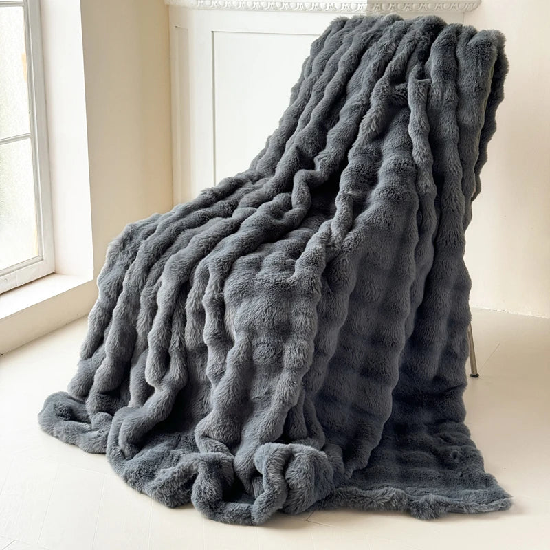 A grey fluffy blanket is draped over a chair in a room with a window.