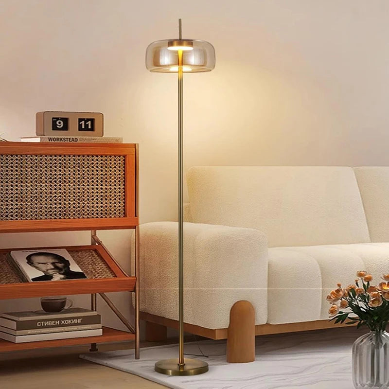 Minimalist gold floor lamp with amber glass shade lit in a warm glow.