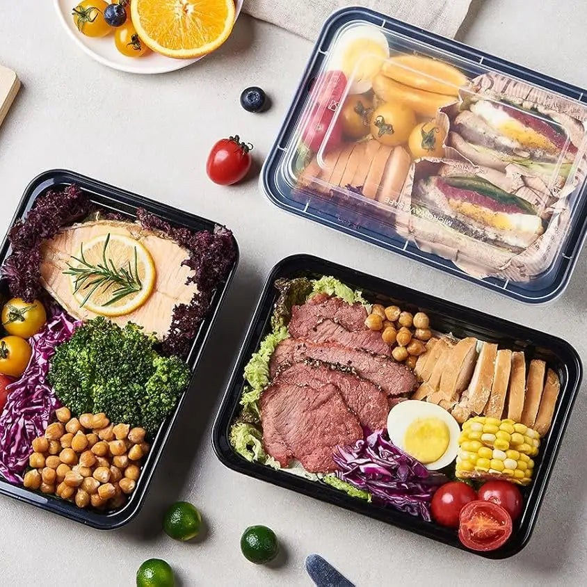 Three black meal prep containers filled with various foods on a light gray surface.