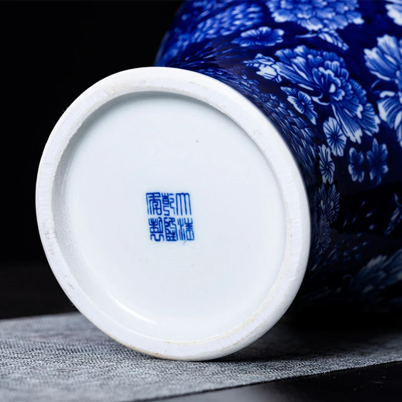 Close-up of the base of a blue and white porcelain vase, showing a blue Chinese seal mark, with part of the floral patterned body visible behind it on a dark background.