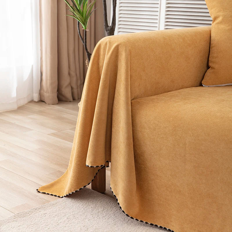 Brown blanket draped over a sofa in a room with curtains and a plant.