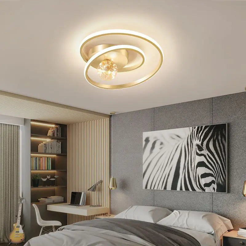 Gold Nordic spiral ceiling light with amber glass globe installed above a modern bedroom with warm ambient lighting