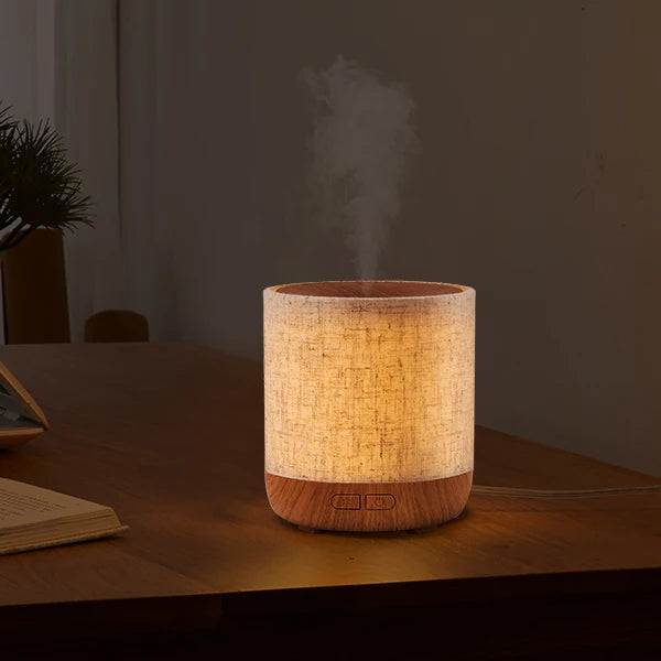 Wooden diffuser emitting steam on a desk with a laptop and books in a room setting