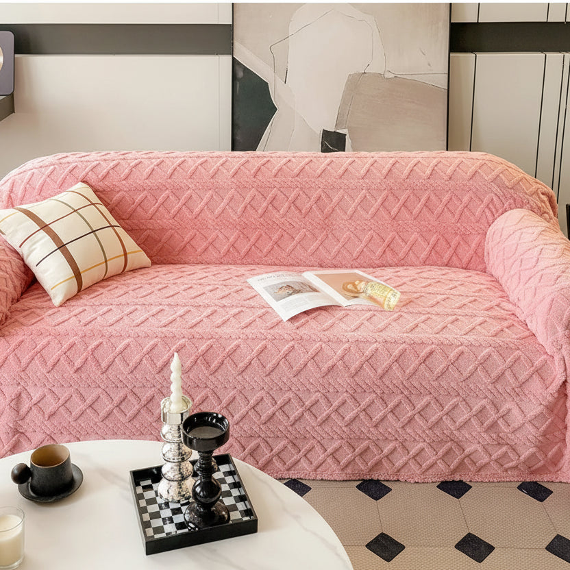 Pink sofa cover with decorative pillows on a couch, surrounded by small items on a table.