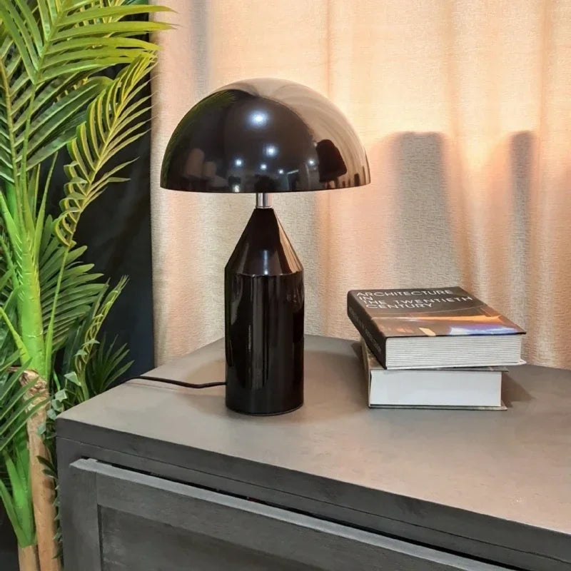 Black table lamp on a surface with books and a plant in the background
