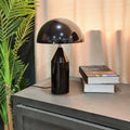 Black table lamp on a surface with books and a plant in the background