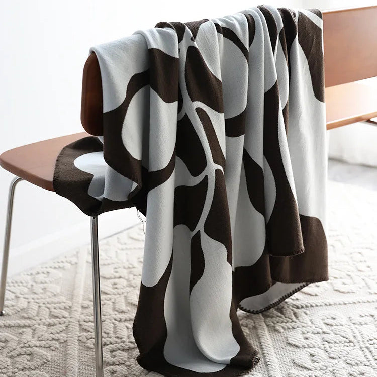 Mocha and grey abstract jacquard blanket draped over a wooden chair on a textured cream rug