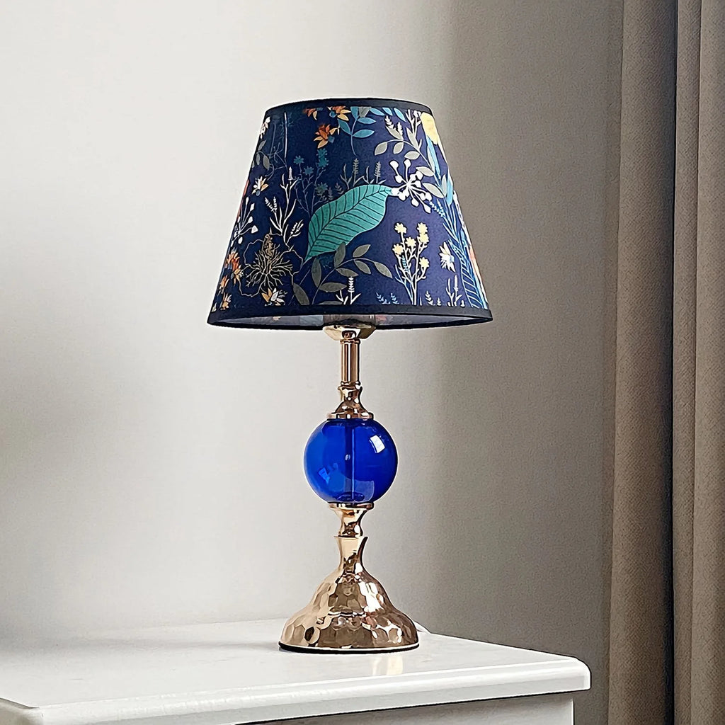 Decorative table lamp with a blue glass base and floral-patterned shade on a white surface.