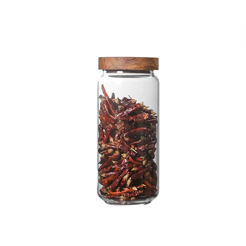 Glass jar with wooden lid filled with red chili peppers on a white background
