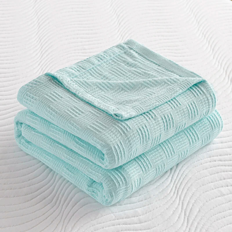 Folded mint green cotton knit blanket with textured basket weave on white quilted surface