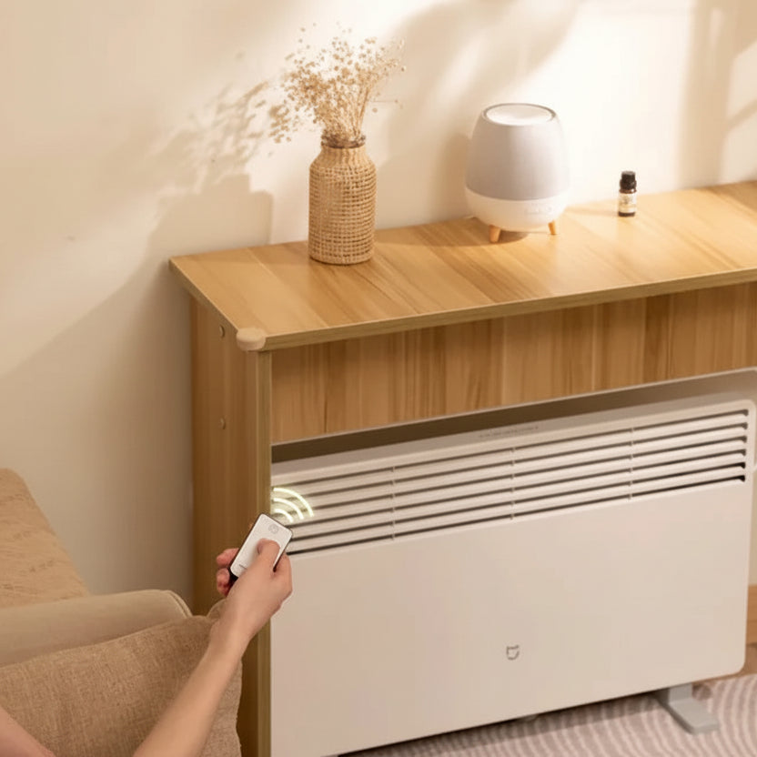 Person using a remote control to adjust a wall-mounted electric heater in a cozy room.