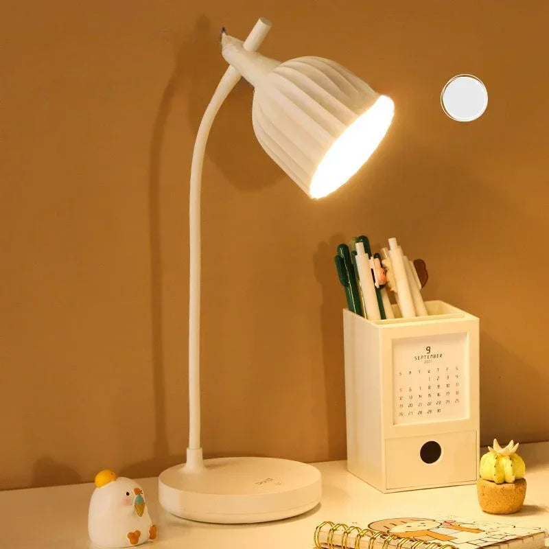 White desk lamp on a desk with a pen holder and small plant