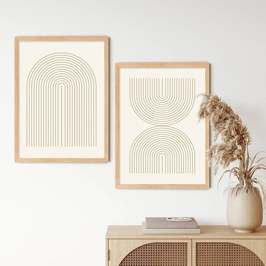 Two abstract line art prints in wooden frames on a white wall with a vase of dried plants.