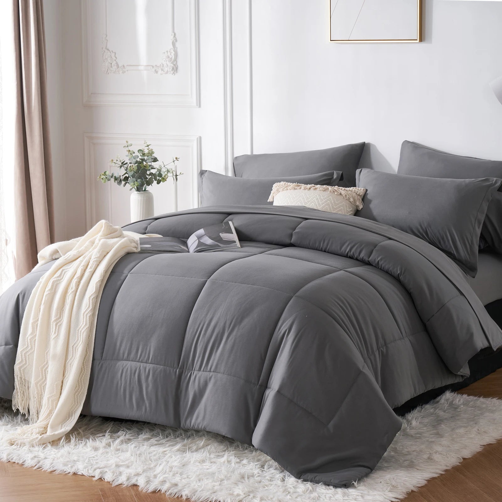 A grey comforter set on a bed in a bedroom with white walls and a window.
