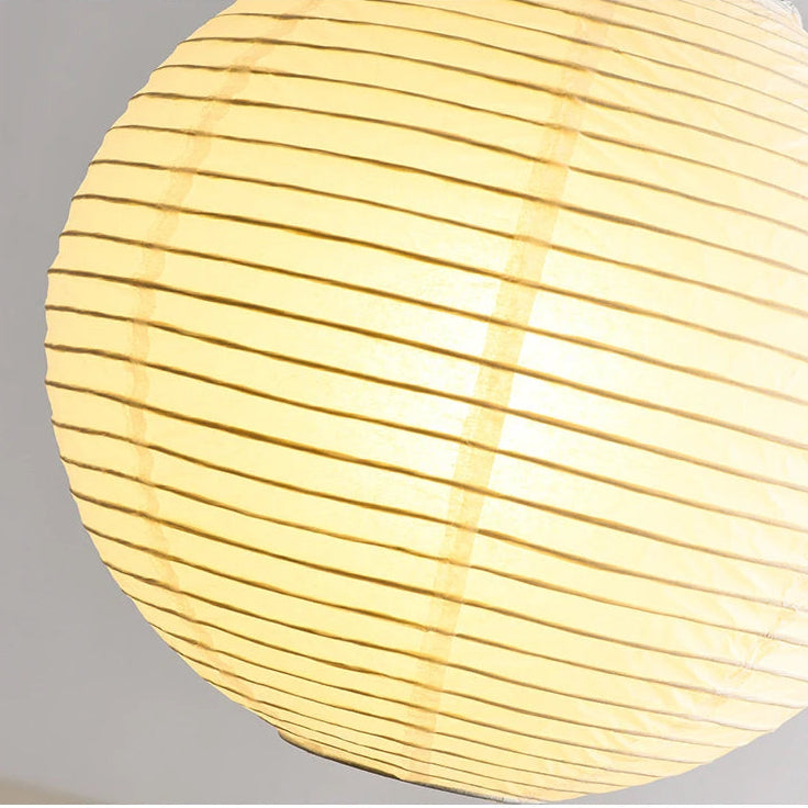 A close-up of a glowing paper lantern with horizontal pleats, emitting a warm yellow light against a neutral gray background.