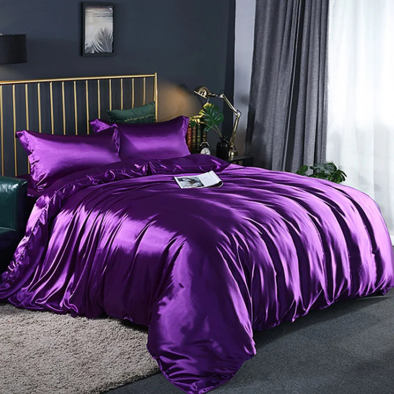 Purple satin bedding set on a bed in a bedroom with gray walls and curtains.