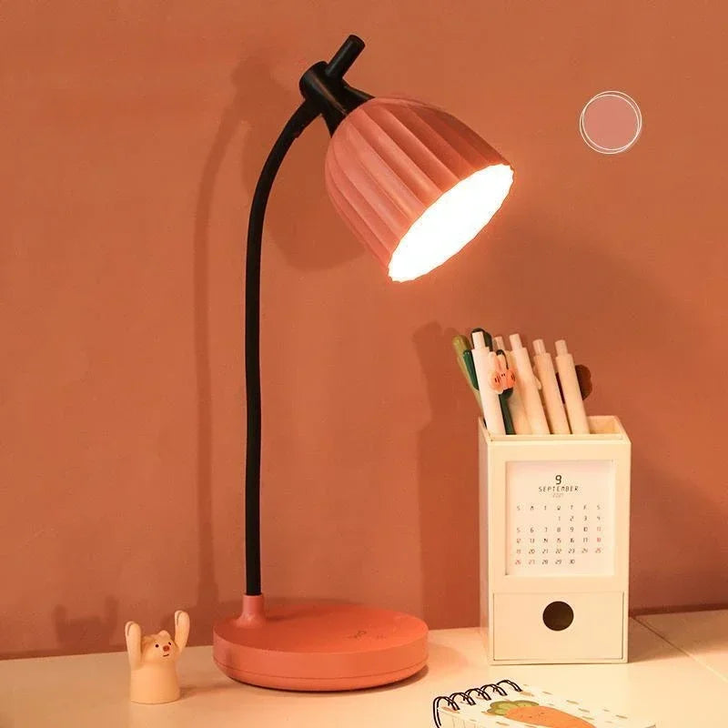 Pink desk lamp on a table with stationery items against a warm-toned wall.