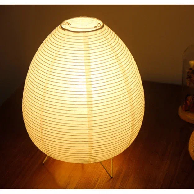 Japanese round lamp emitting a warm glow on a wooden surface with plants in the background