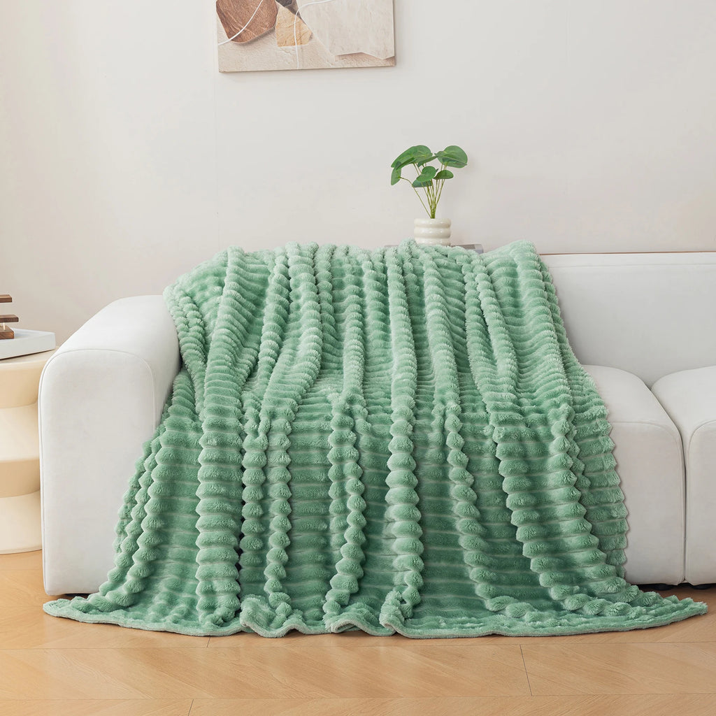 Green textured blanket draped over a white sofa in a living room setting.