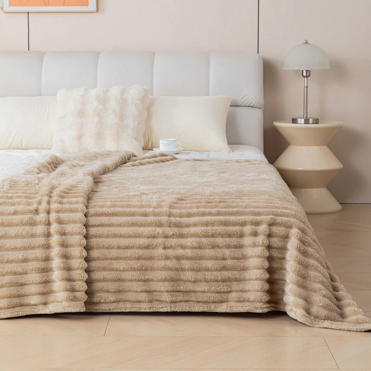 Beige textured blanket on a bed in a bedroom setting with a lamp and nightstand.
