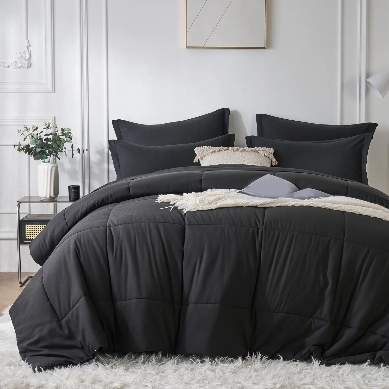 Black comforter set on a bed in a bedroom with white walls and decor.