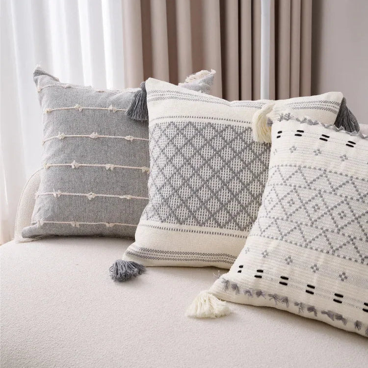 Three patterned cushions on a sofa with a lamp and curtains in the background.