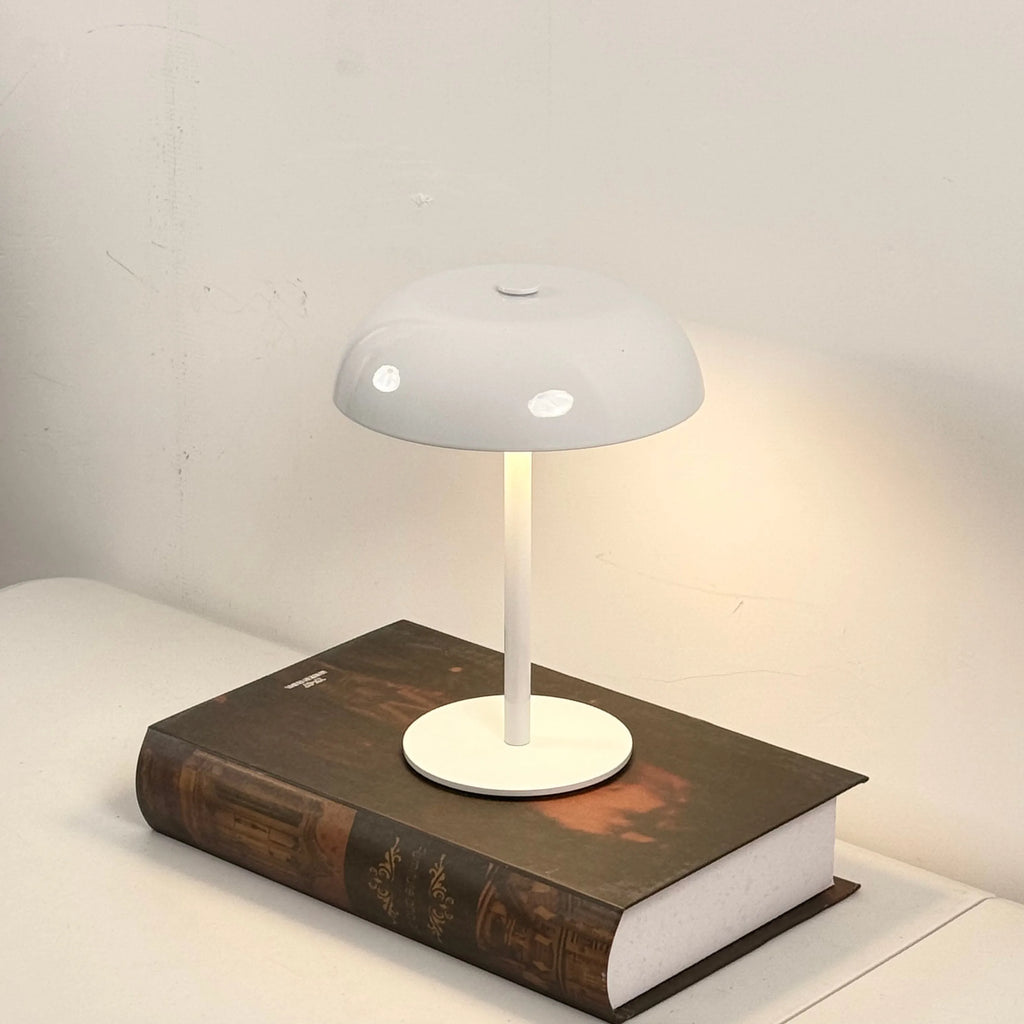 Modern white mushroom lamp with white base and shade on a book against a plain background