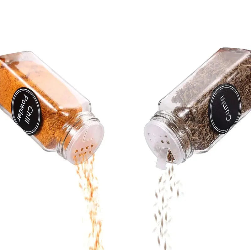 Two clear spice shakers with spices being poured out on a white background.